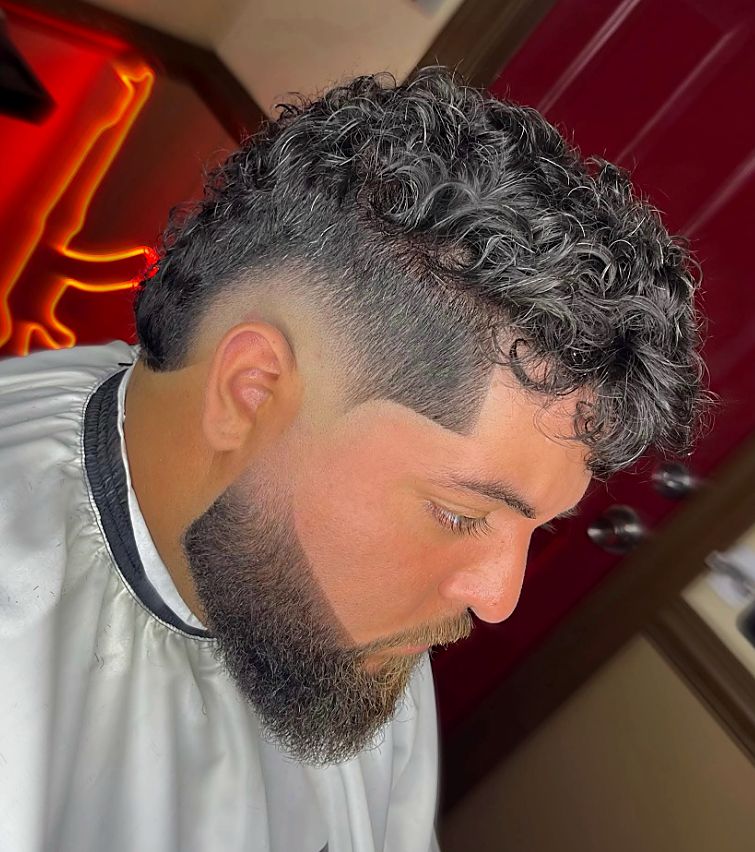 Curly top with a low taper fade and sculpted beard