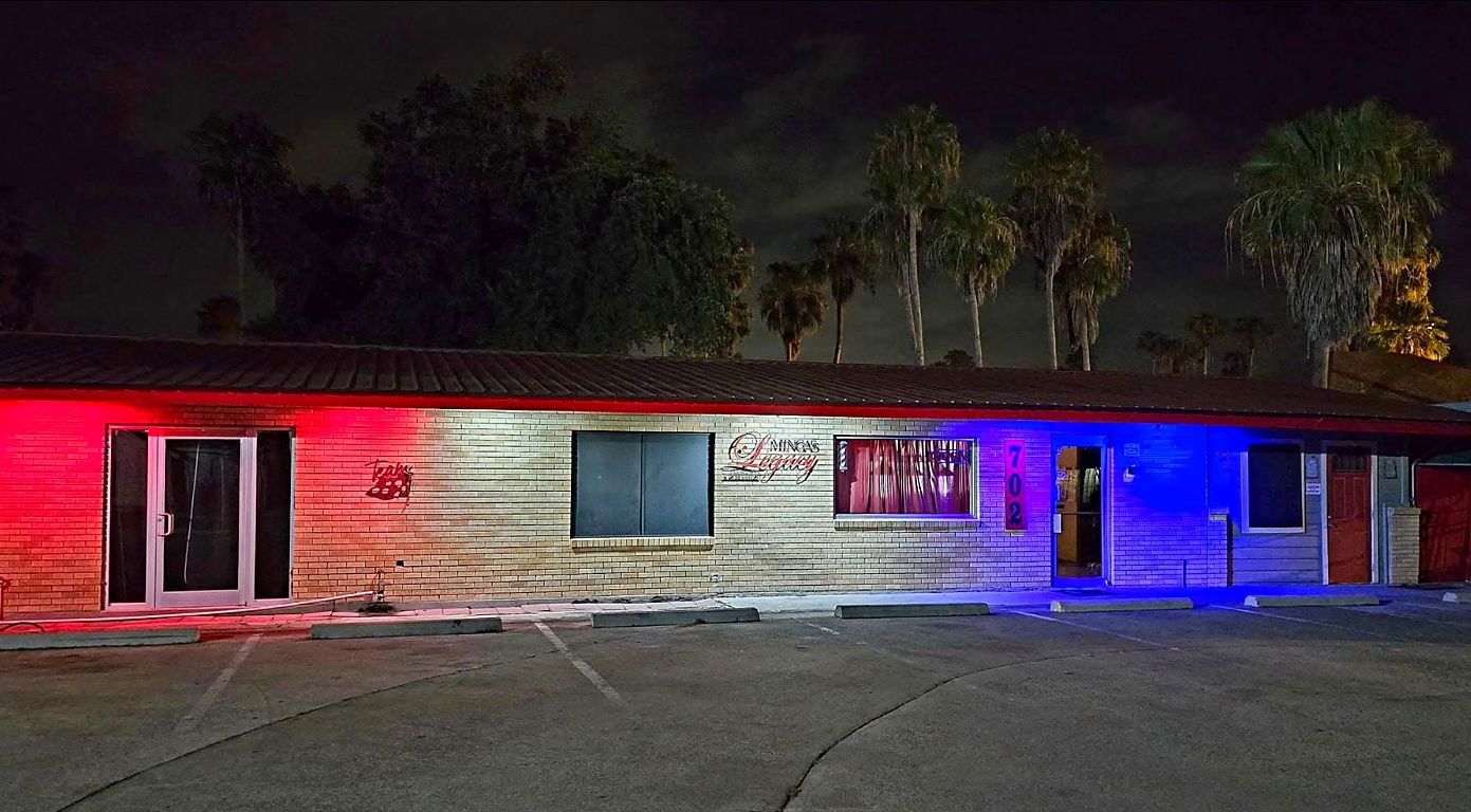 Minga's Legacy storefront at night, lit in red and blue, at 702 S Pleasantview Dr, Weslaco